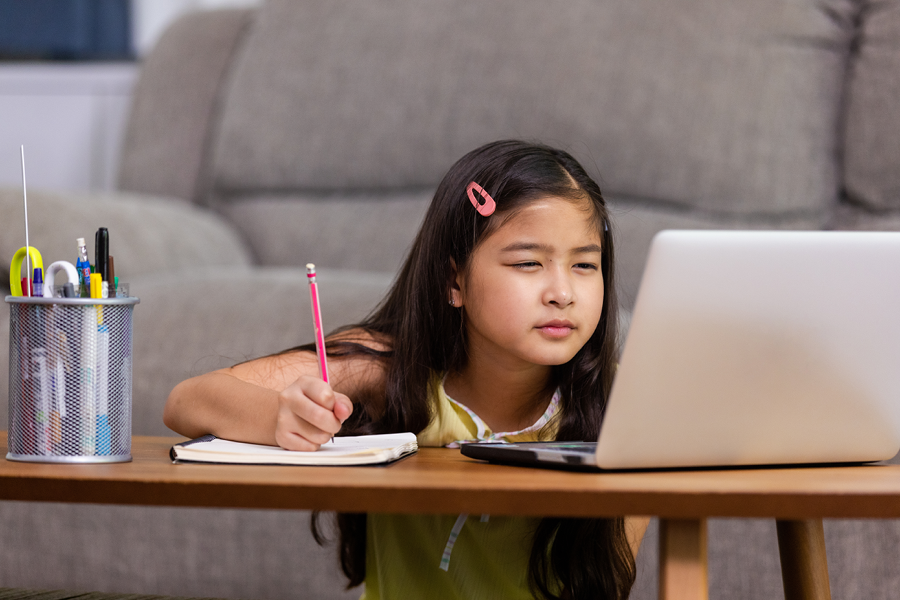 Child taking notes from her computer to a notebook.