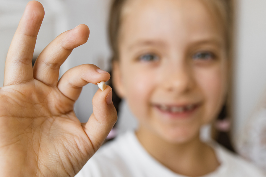 Child smiling and holding their baby tooth.