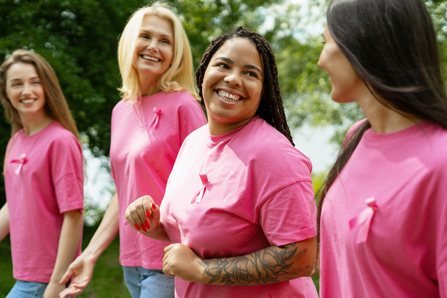 Group of women smiling and laughing while wearing pink and breast cancer ribbons.