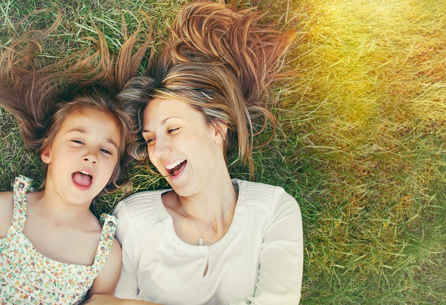 Mother and daughter smiling in the sun and laying in the grass
