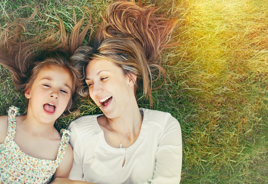 Mother and daughter smiling in the sun and laying in the grass.