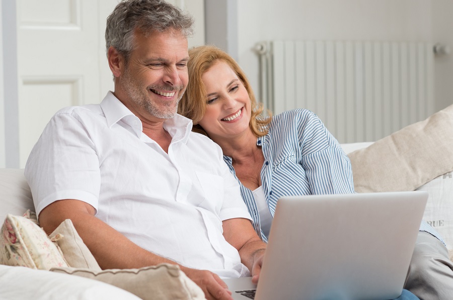 Middle aged couple sitting on couch enjoying something on their computer