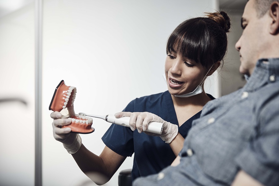 Dentist showing older man patient how to brush their teeth