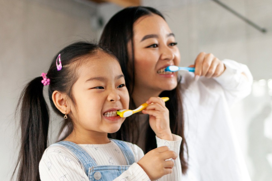 mother teaching her daughter how to brush her teeth