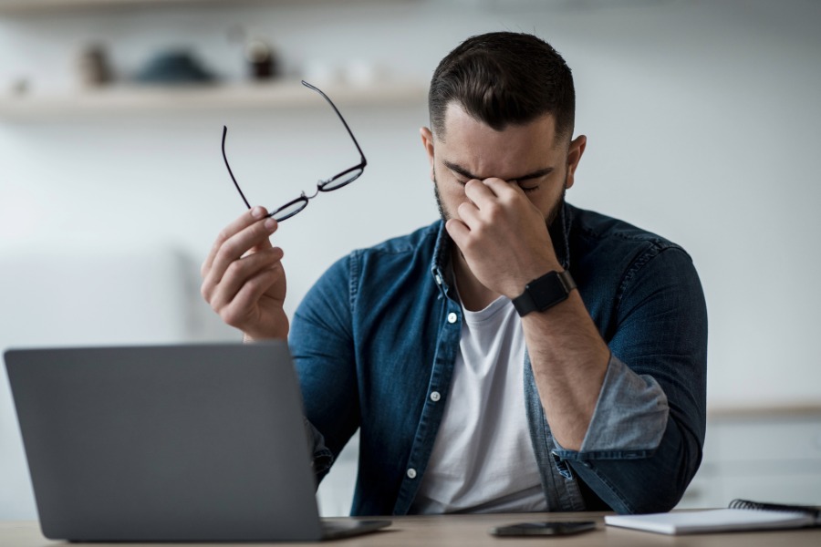 man sitting at computer rubbing his eyes