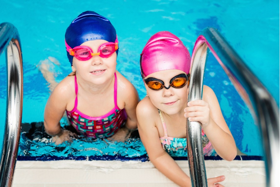 two kids swimming in a pool wearing goggles and swim caps
