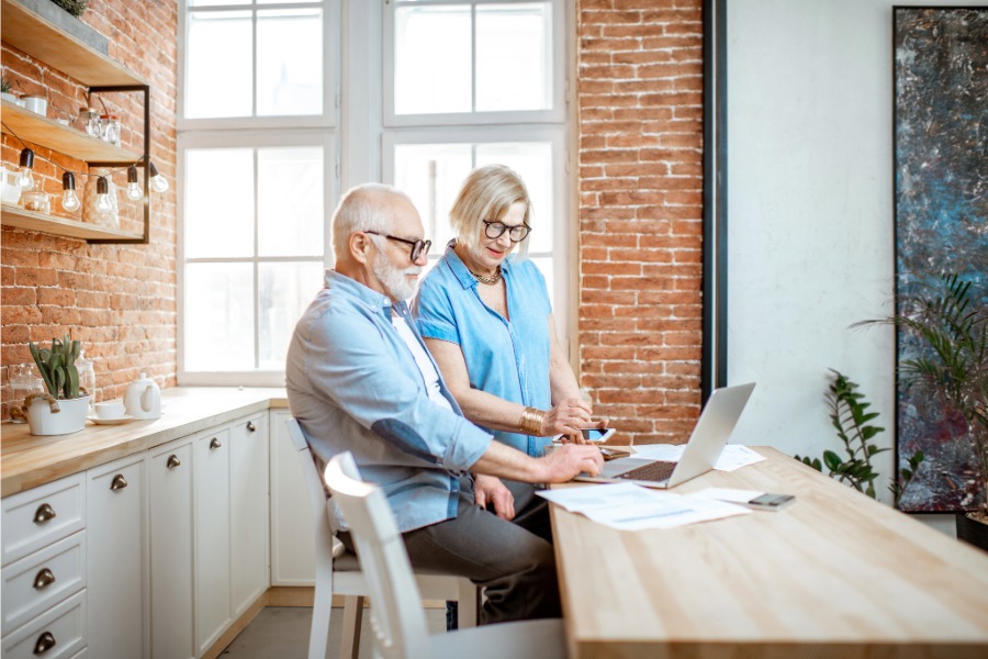 senior man and woman reviewing papers and looking at laptop