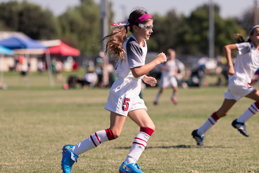 Girl playing soccer with protective glasses