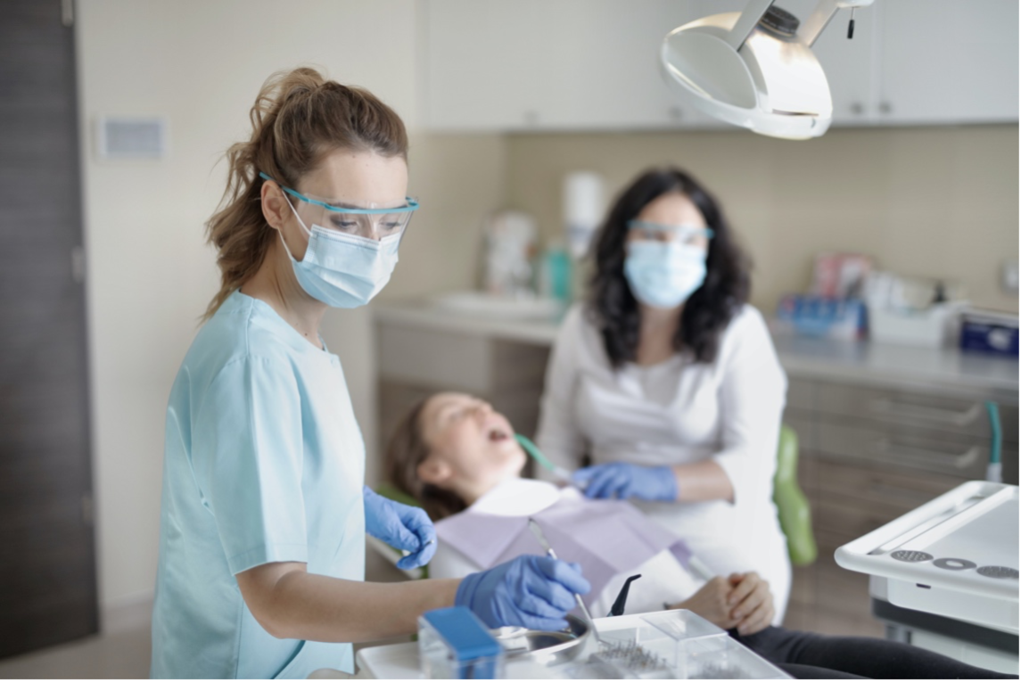 A dentist and his dental assistant make a young female patient laugh in the dental chair.
