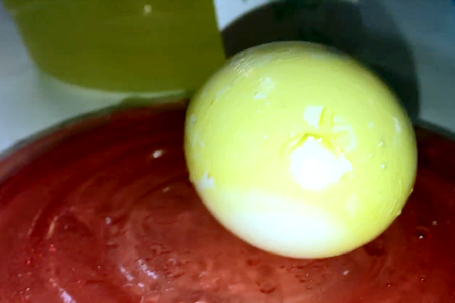 An eggshell is stained bright yellow and peels after soaking in lemon lime soda overnight.