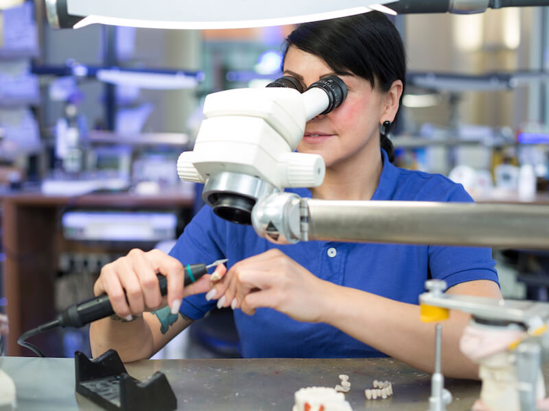 Dental technician producing a prosthesis under a microscope