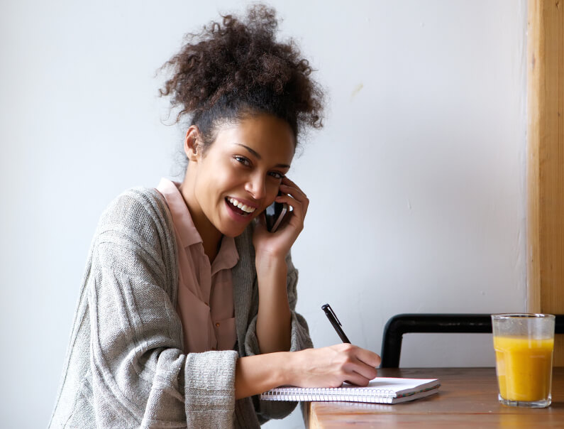 Young woman calling by phone and writing in notebook